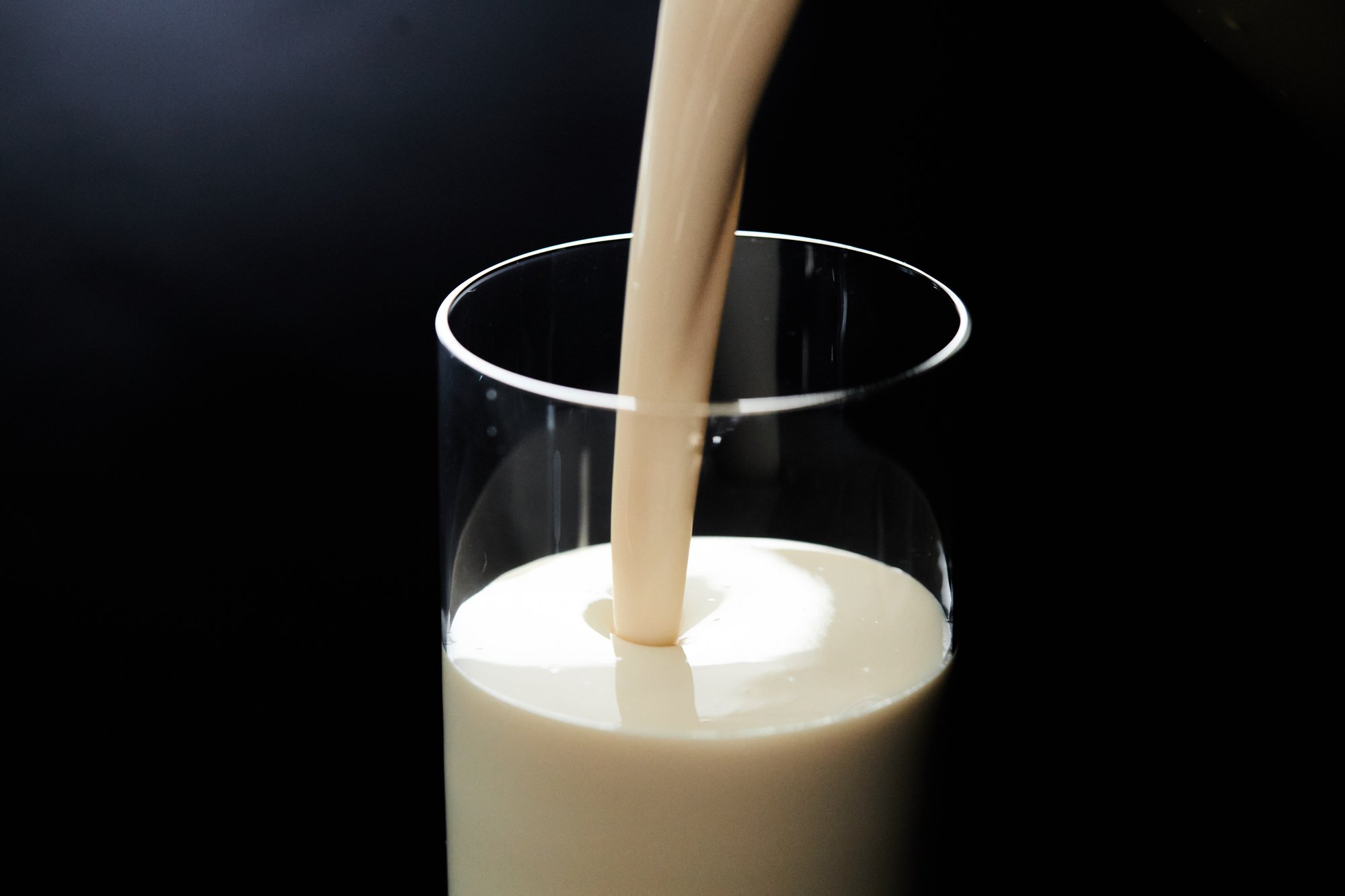 Creamy vanilla ready-to-drink beverage being poured into clear glass on black background.