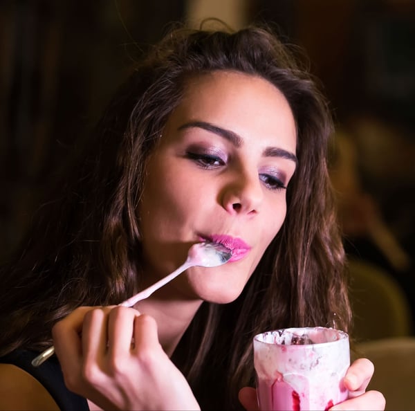 Woman with spoon in mouth holding protein yogurt in a glass